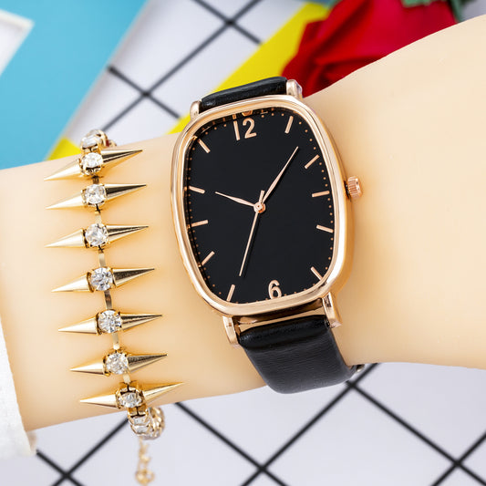 Gold watch with black face and black strap worn on a wrist with a colorful background